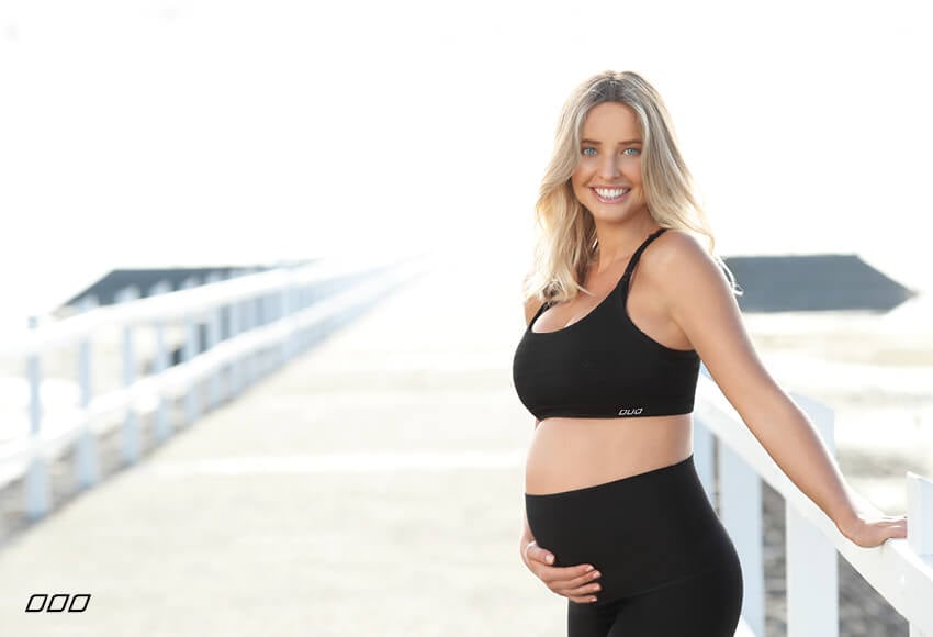Pregnant model wearing black breastfeeding sports bra and black maternity leggings