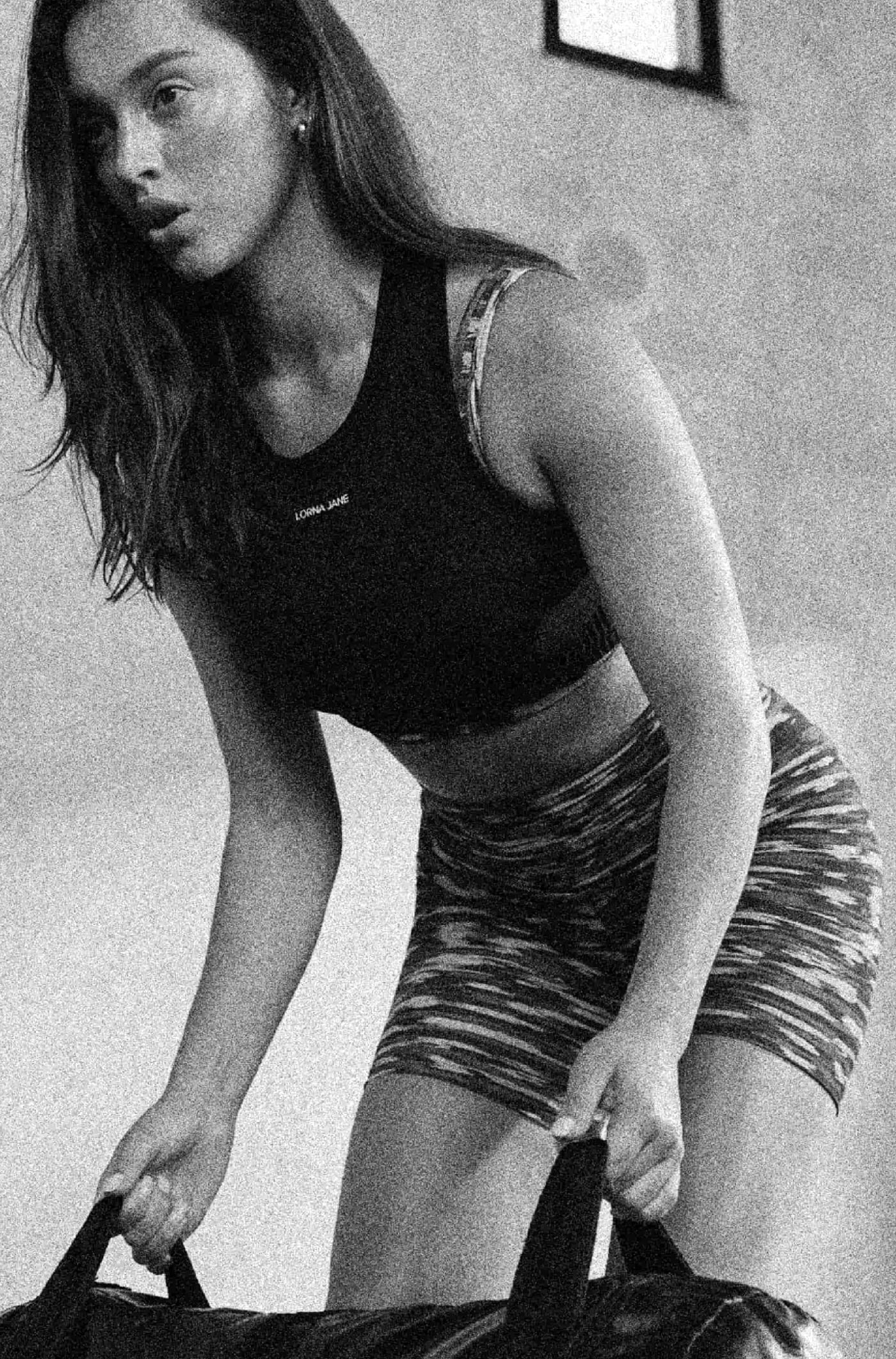 A close up front shot of a model lifting a weighted bag wearing lorna jane black top and rib shorts.