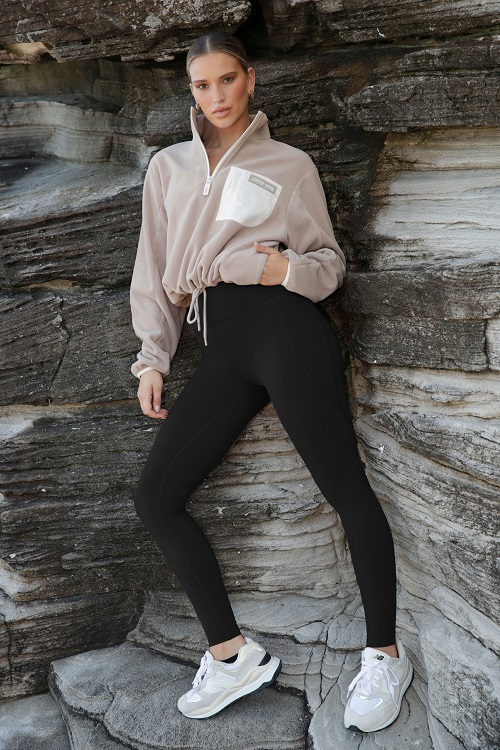 woman leaning on a rock wall wearing black thermal leggings and a two tone tan sweater