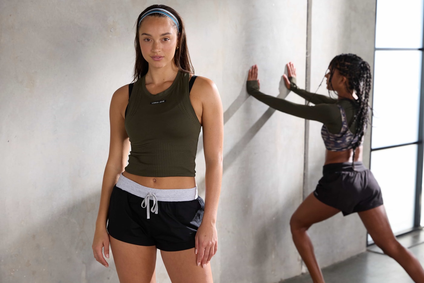 Front Image of a model wearing shorts and a green crop top with a model behind her leaning against a wall in black and green activewear.