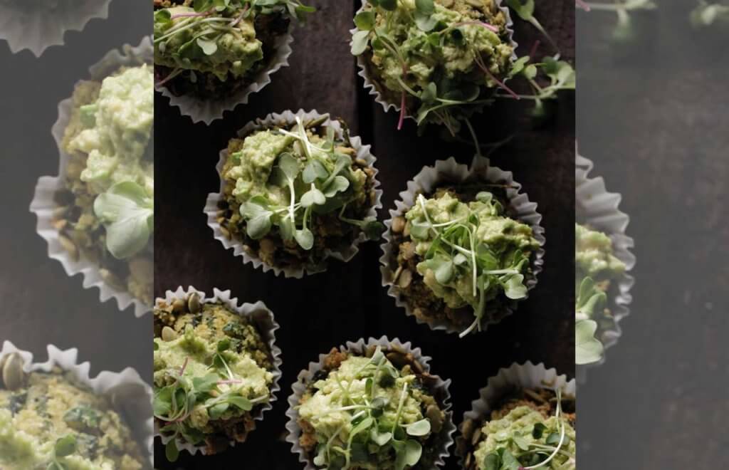 spinach kale and chia muffins freshly baked, topped with avocado and alfalfa sitting on wooden bench top